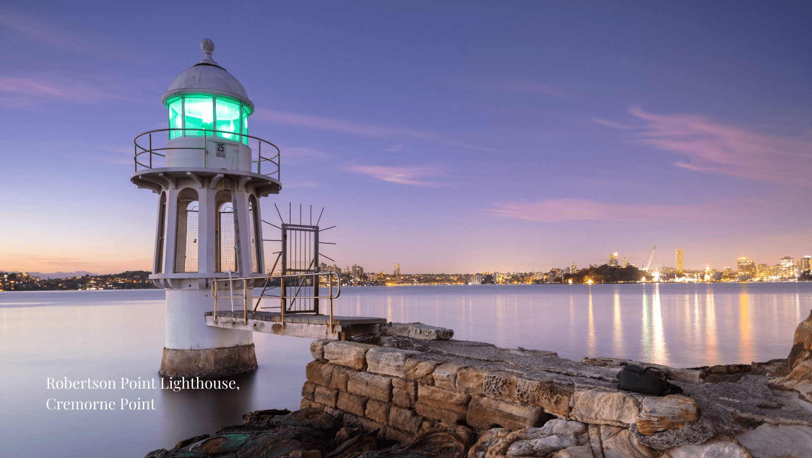 Robertson Point Lighthouse at Cremorne Point at dusk, with the city lights across the harbour