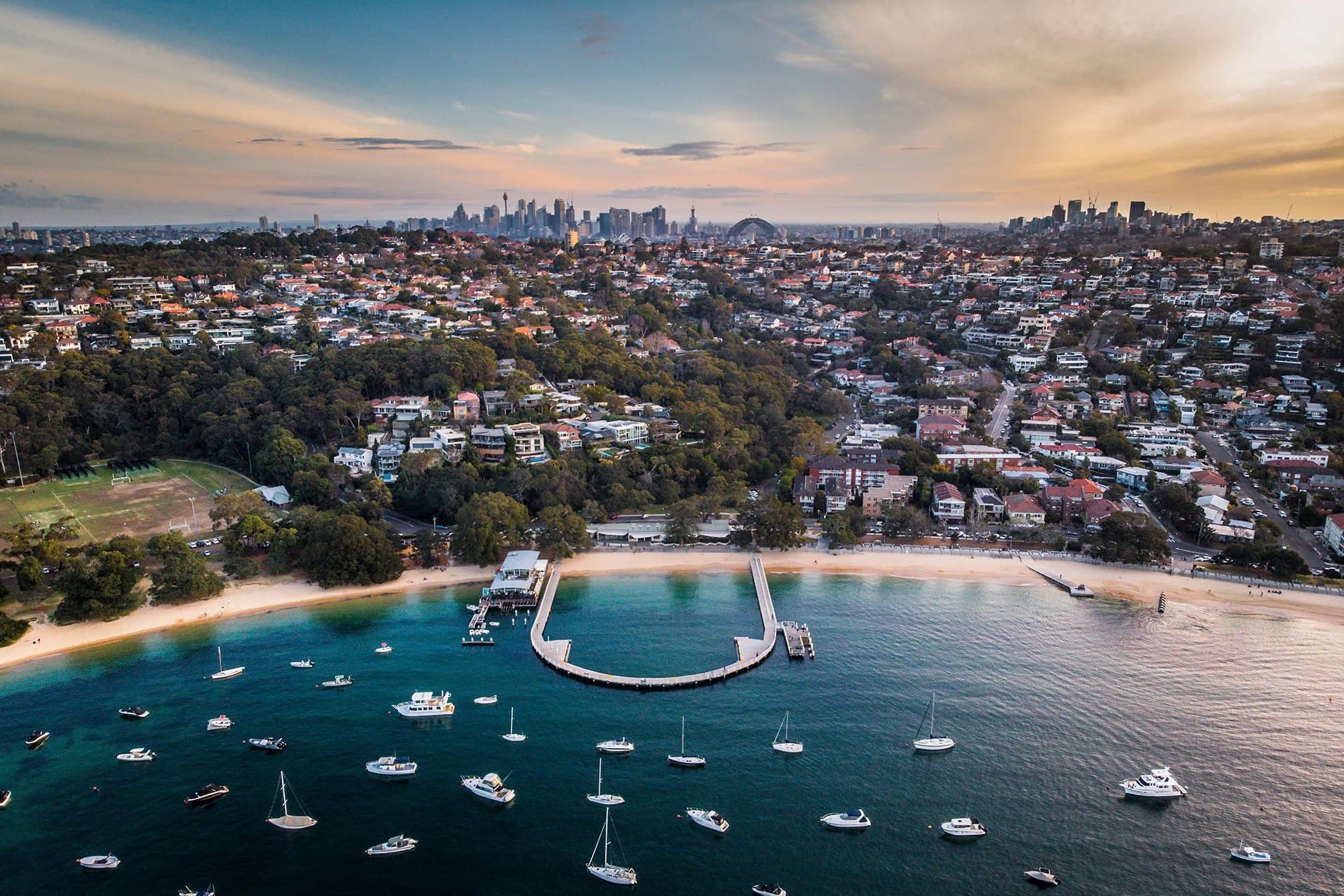Aerial view of Balmoral Beach in Mosman at sunset, with the Sydney CBD and Harbour Bridge on the horizon